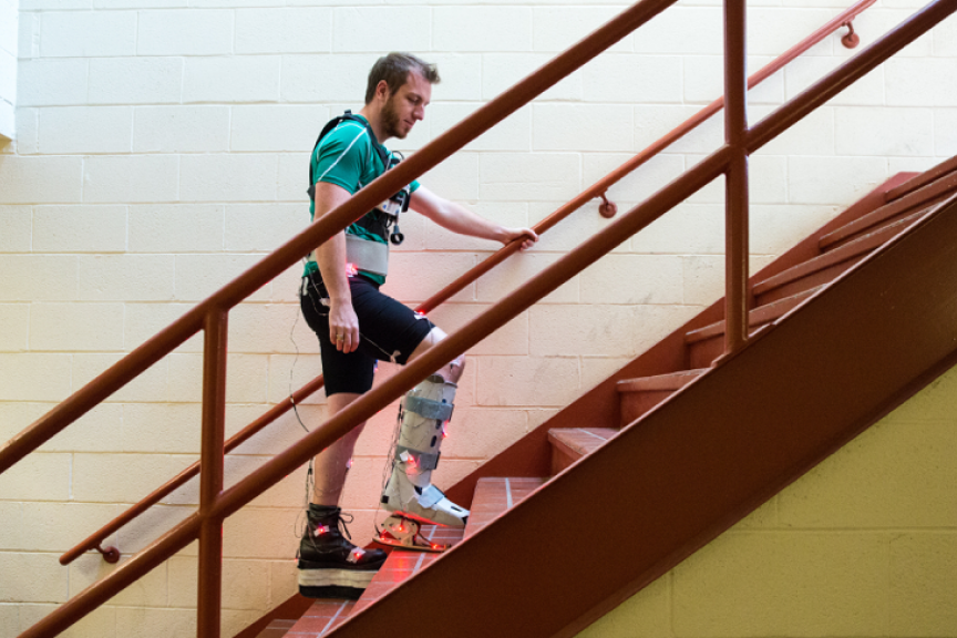 A man wearing an assisted movement device on his right leg walks up a flight of stairs