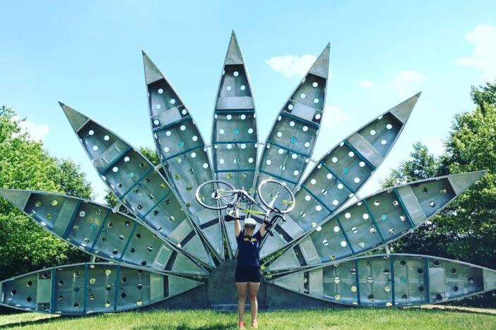Brooke Donovan holding up a bike in front of a sculpture