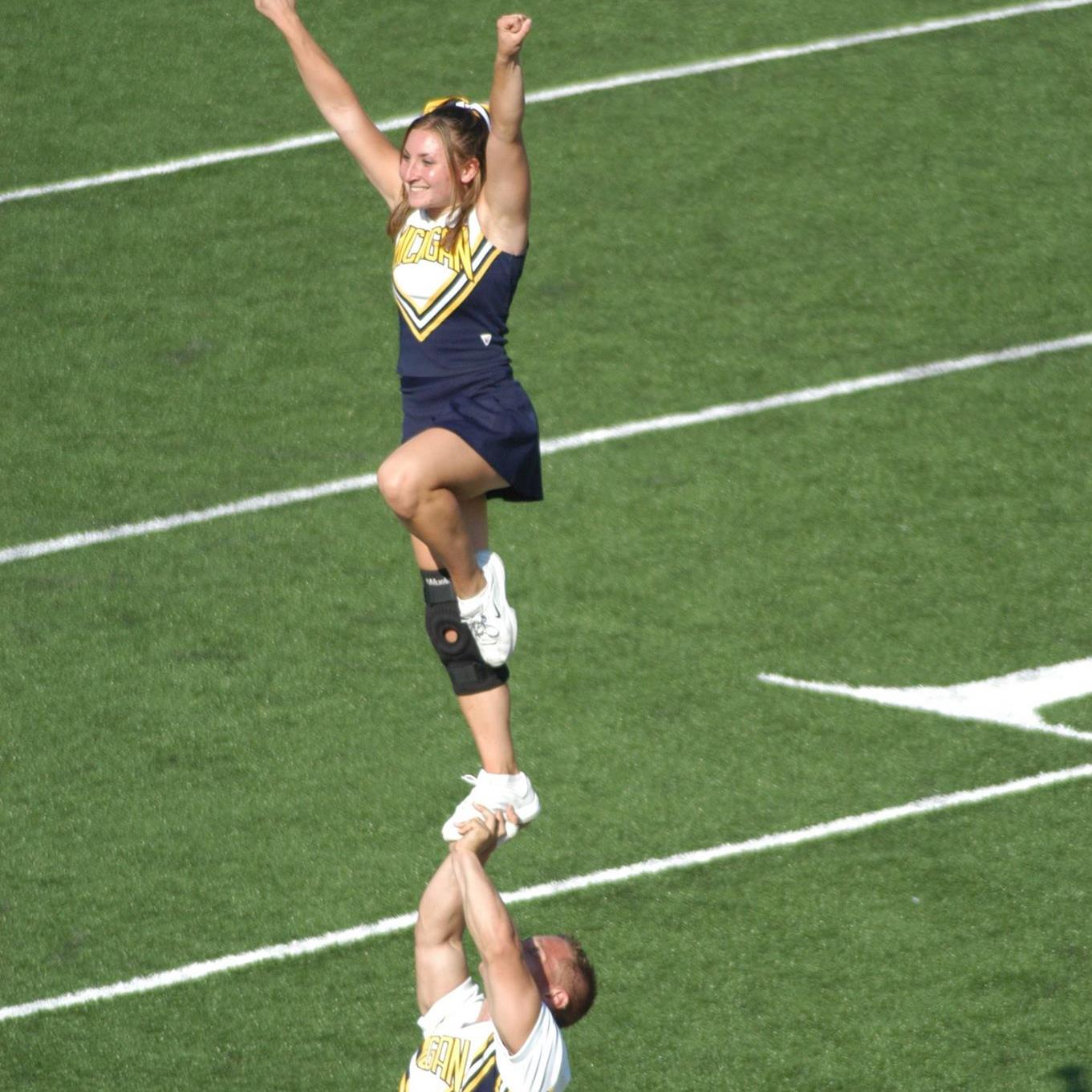 A person standing up on someone else's foot in a Michigan cheerleading uniform