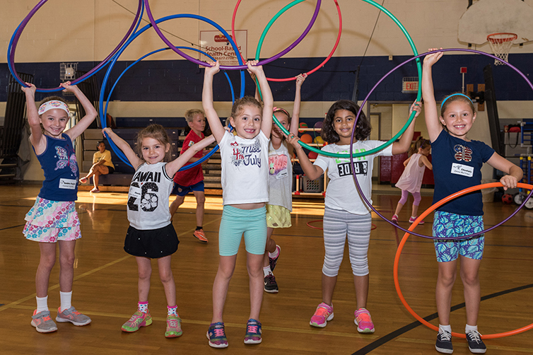 Girls raising hula hoops over their heads in a gym