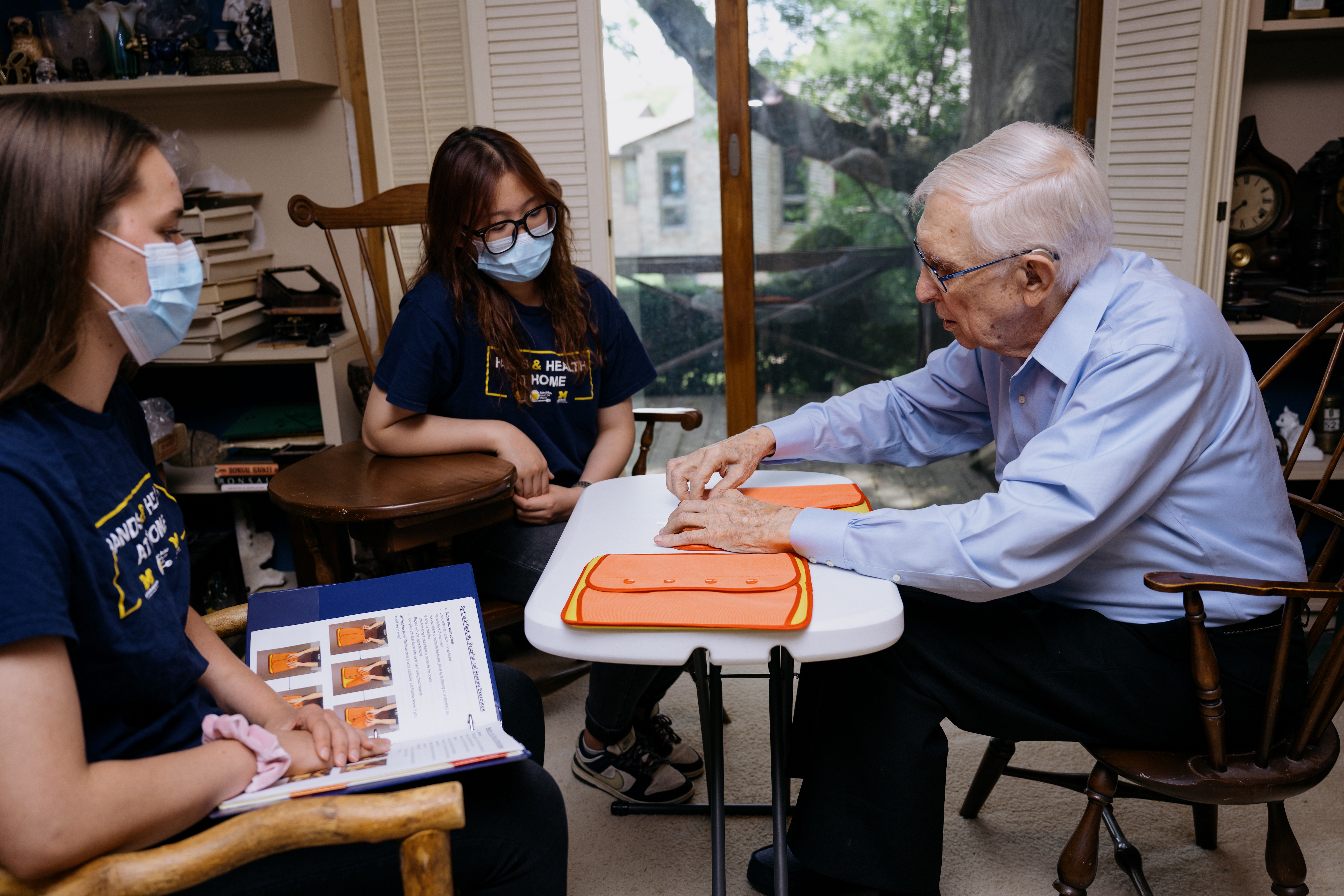 Two master's students observe as a Hands and Health at Home participant practices buttoning on a sample button board.