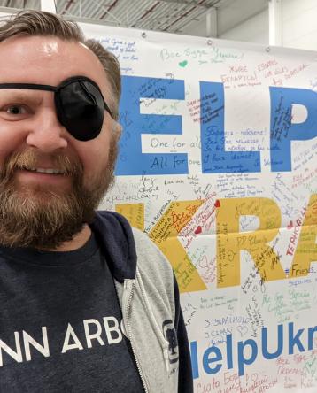 Mike Lorenc with an eye patch in front of a sign that reads, &quot;Help Ukraine&quot;