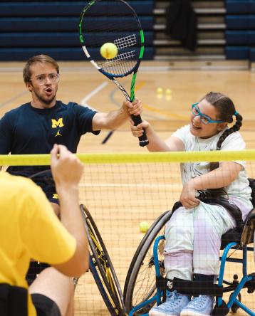 Chris Kelley shows an adaptive athlete how to hit a tennis ball.
