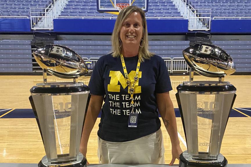 Jodi Tye stands between two trophies on a basketball court.