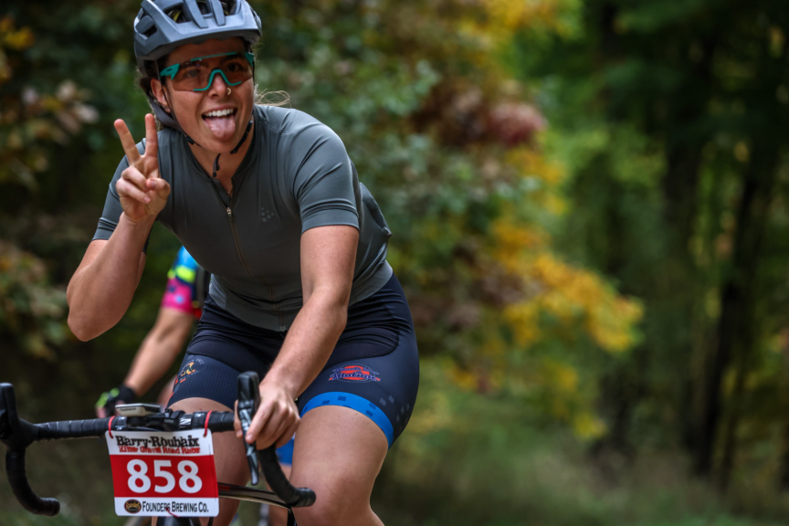 Bhillie Luciani on a bike during a race giving a peace sign and sticking out her tongue