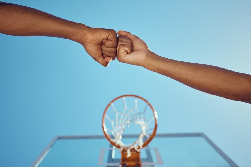 Two people fist bumping under a basketball hoop
