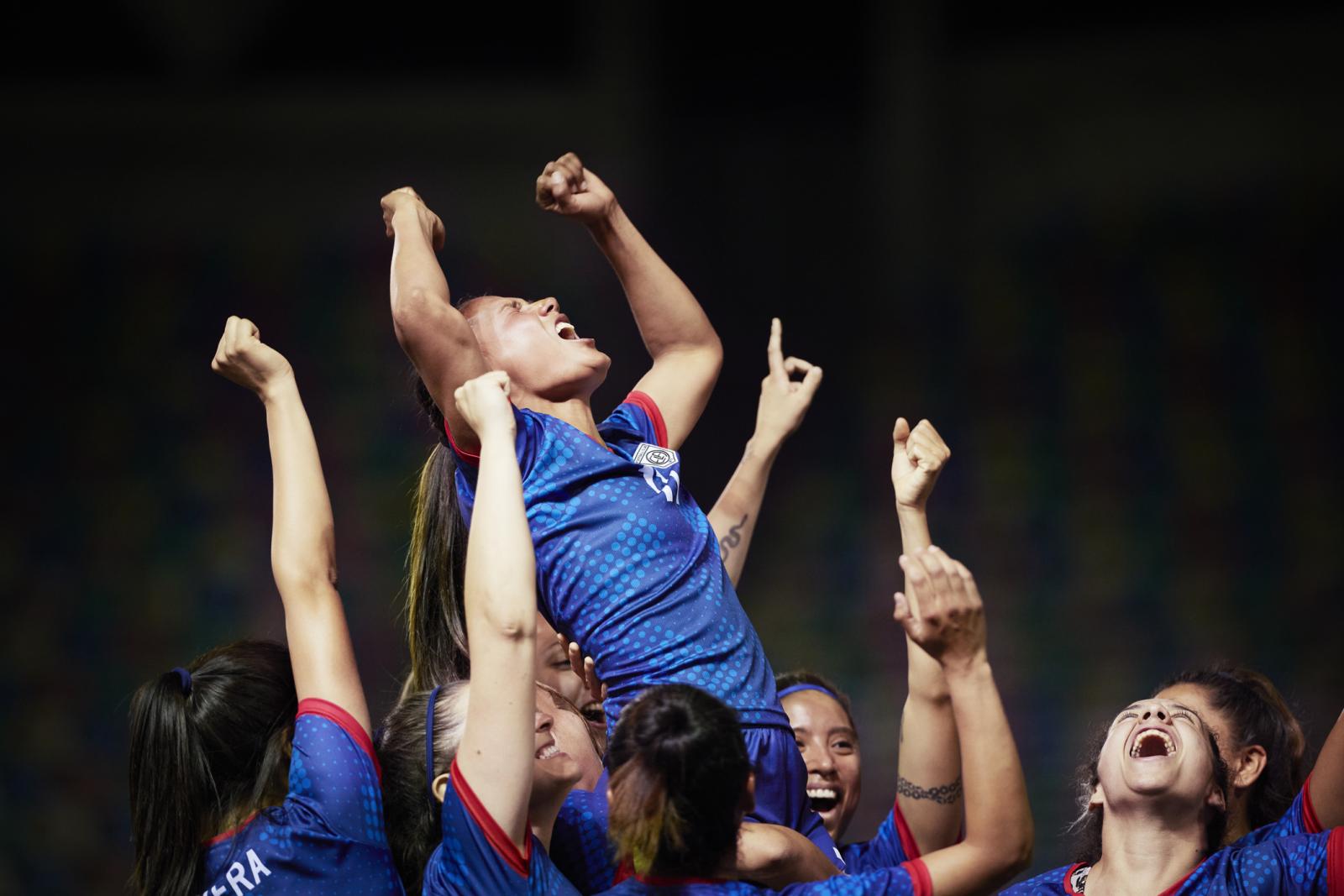 A group of female soccer players celebrate, lifting one player on their shoulders and throwing their arms in the air.