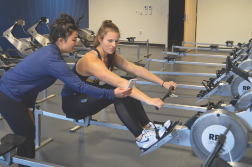 A movement science student shows a young woman on a rowing machine her smart phone