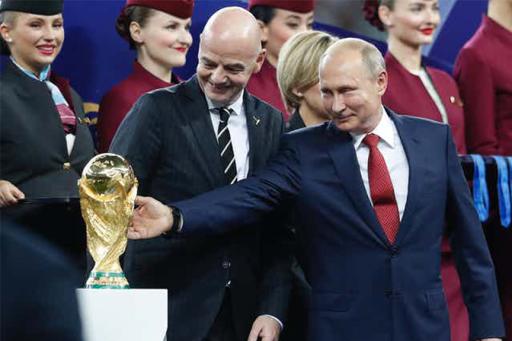 Vladimir Putin holding arm out touching World Cup trophy with FIFA president by his side.