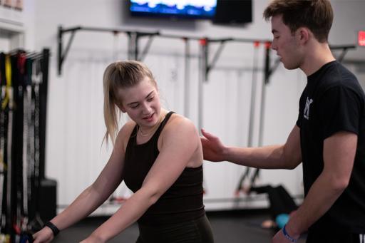 Female student working out under the instruction of a male student.