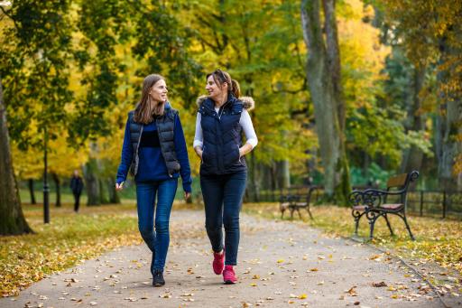 Two women dressed in warm clothing walking in a park during fall