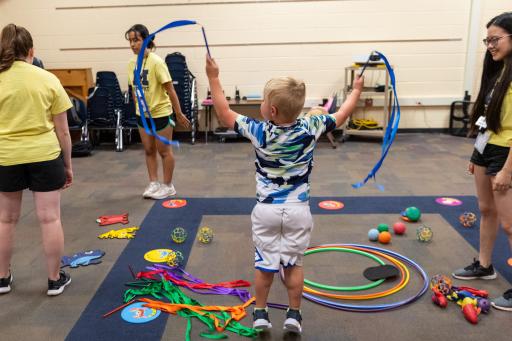 KidSport Adaptive camper Joey plays with blue streamers while counselor Shanan Sun looks on.