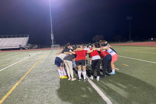Female athletes join together in a circle on the soccer field