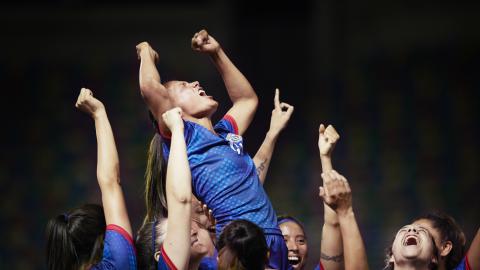 A group of female soccer players celebrate, lifting one player on their shoulders and throwing their arms in the air.